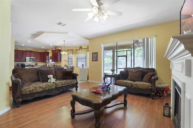 living room with baseboard heating, ceiling fan, and light wood-type flooring