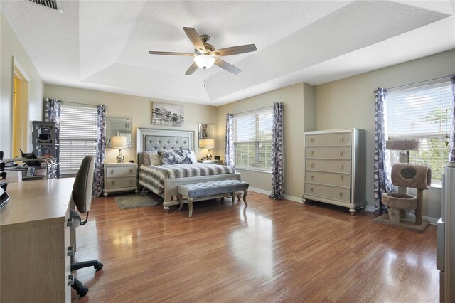 bedroom with dark wood-type flooring, a tray ceiling, ceiling fan, and a textured ceiling