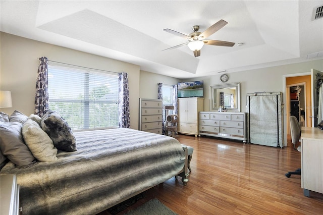 bedroom featuring a raised ceiling, wood-type flooring, and ceiling fan