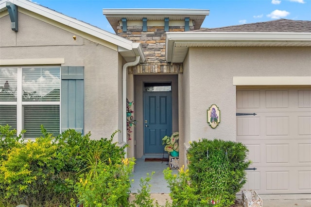 view of exterior entry featuring an attached garage, stone siding, and stucco siding