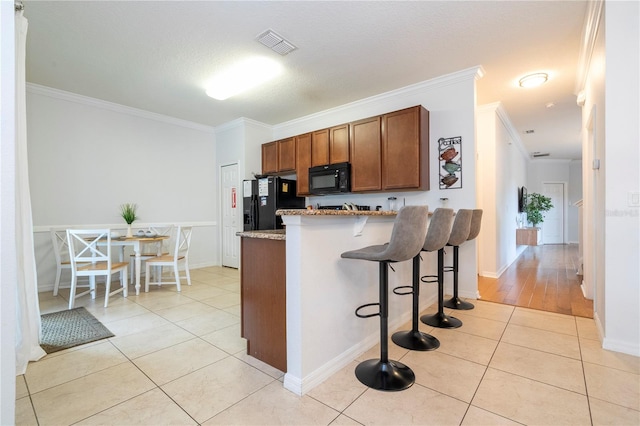 kitchen featuring light tile patterned floors, ornamental molding, a kitchen breakfast bar, and black appliances