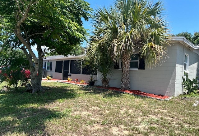 view of property exterior featuring a sunroom, concrete block siding, and a lawn