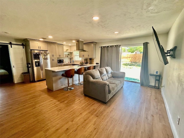 living room with a textured ceiling, a barn door, baseboards, and light wood-style floors