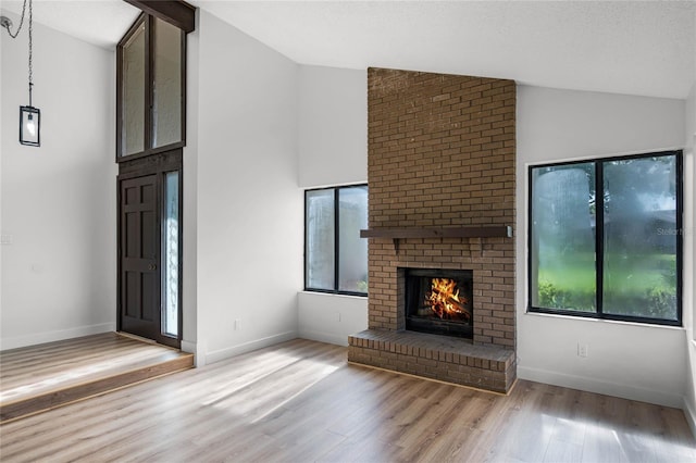 unfurnished living room featuring high vaulted ceiling, a brick fireplace, wood finished floors, and baseboards