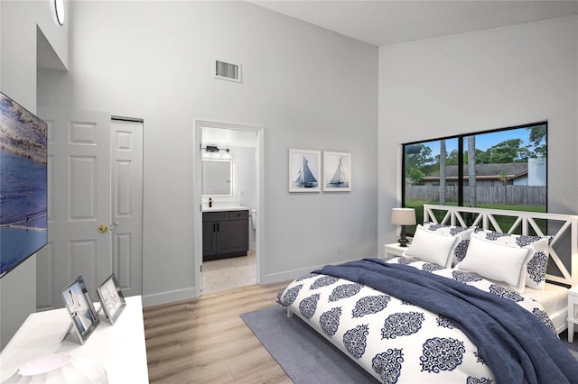 bedroom with ensuite bathroom, light wood-style flooring, a high ceiling, visible vents, and baseboards