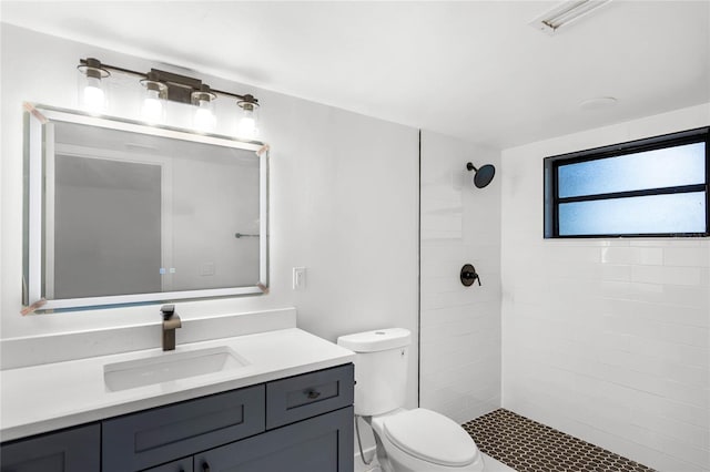 bathroom featuring a tile shower, vanity, and toilet