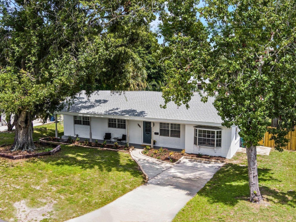 single story home with driveway, a shingled roof, fence, a front yard, and brick siding