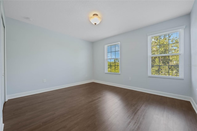 spare room with baseboards and dark wood finished floors