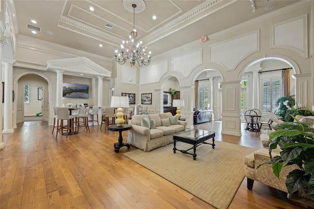 living room featuring crown molding, ornate columns, a notable chandelier, and light hardwood / wood-style floors