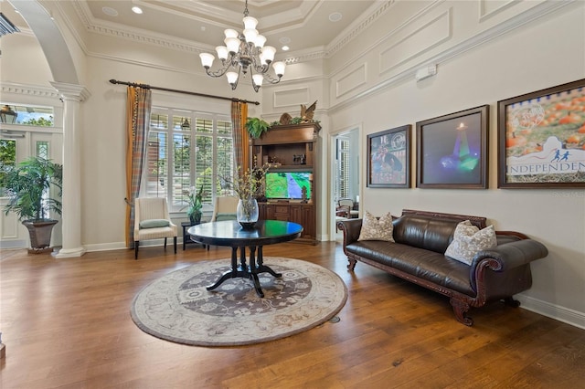 living area featuring decorative columns, a raised ceiling, crown molding, and wood finished floors