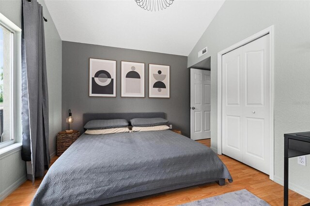 bedroom featuring a closet, light hardwood / wood-style floors, vaulted ceiling, and multiple windows