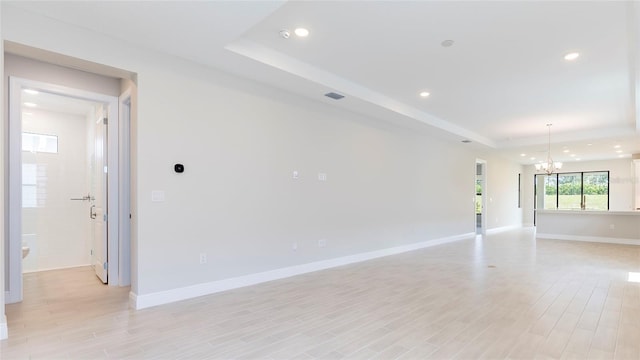 unfurnished room with a tray ceiling, light hardwood / wood-style flooring, and a notable chandelier