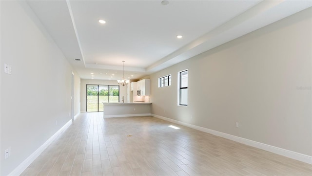 unfurnished living room with a tray ceiling, light hardwood / wood-style floors, and a notable chandelier