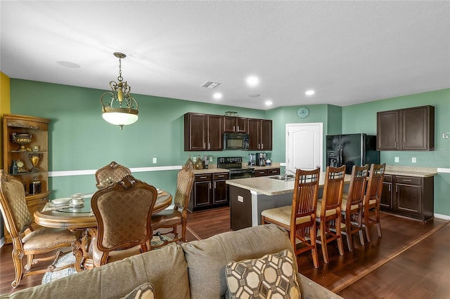 kitchen with black appliances, pendant lighting, dark hardwood / wood-style floors, and an island with sink