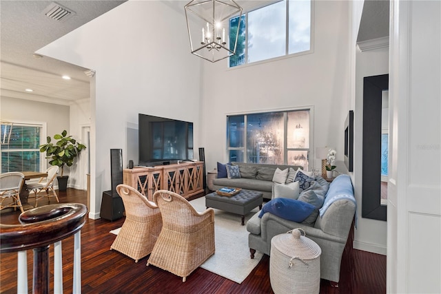 living room with dark wood-type flooring, ornamental molding, a towering ceiling, and an inviting chandelier