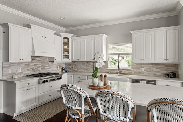 kitchen featuring a textured ceiling, custom exhaust hood, white cabinetry, stainless steel gas stovetop, and crown molding