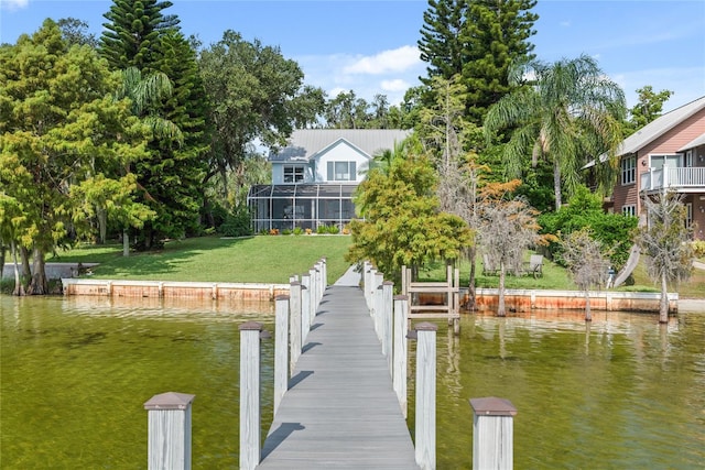 view of dock with glass enclosure, a yard, and a water view