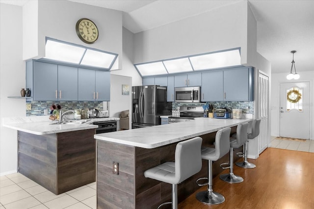 kitchen with a breakfast bar area, appliances with stainless steel finishes, a sink, blue cabinets, and a peninsula