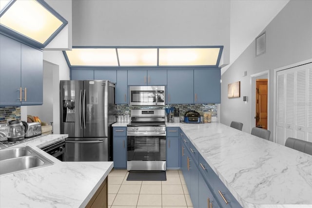 kitchen with blue cabinetry, backsplash, appliances with stainless steel finishes, a sink, and a peninsula