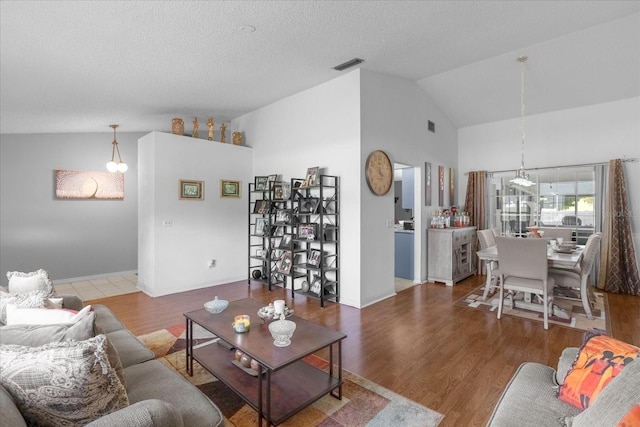 living area featuring visible vents, vaulted ceiling, a textured ceiling, and wood finished floors