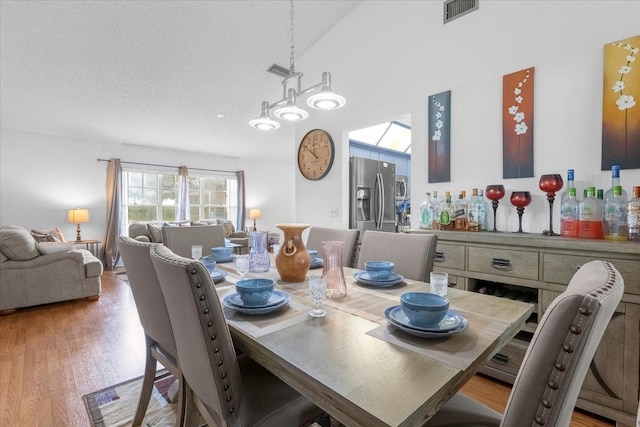 dining area featuring a textured ceiling, vaulted ceiling, light wood-type flooring, and visible vents