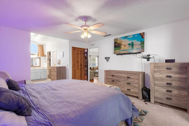 carpeted bedroom featuring a ceiling fan, visible vents, a textured ceiling, and ensuite bathroom