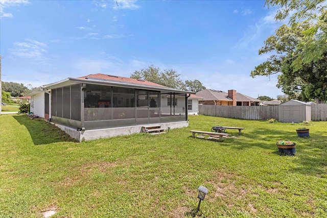 rear view of house featuring an outbuilding, a yard, a sunroom, fence, and a shed