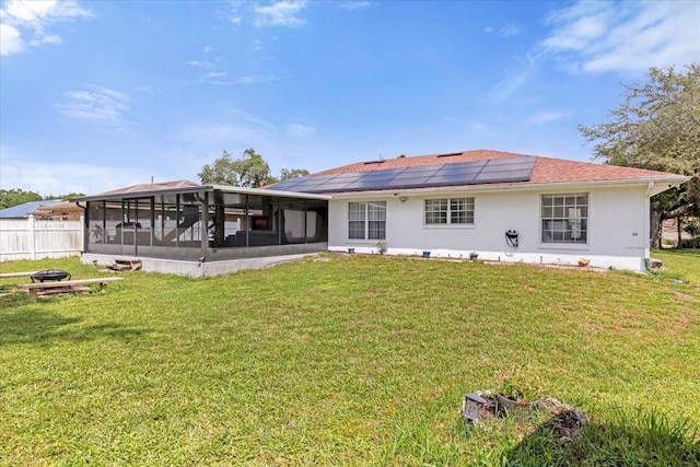 back of house with a sunroom, a lawn, roof mounted solar panels, and stucco siding