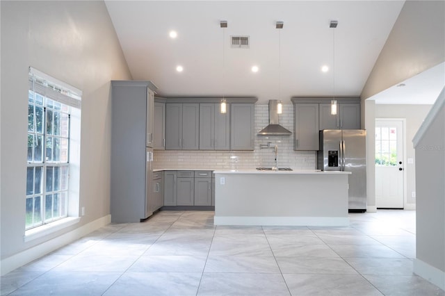 kitchen with tasteful backsplash, decorative light fixtures, a center island with sink, gray cabinetry, and wall chimney range hood