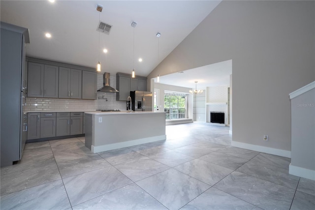 kitchen featuring hanging light fixtures, stainless steel refrigerator with ice dispenser, a brick fireplace, and a kitchen island with sink