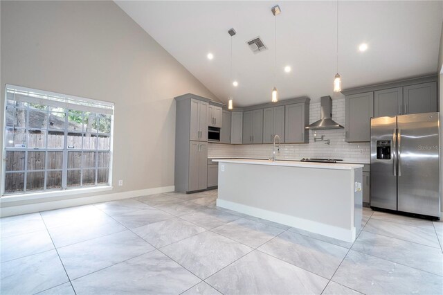 kitchen featuring decorative light fixtures, a center island with sink, tasteful backsplash, stainless steel appliances, and wall chimney range hood