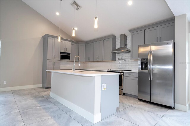 kitchen with wall chimney range hood, appliances with stainless steel finishes, a center island with sink, and vaulted ceiling