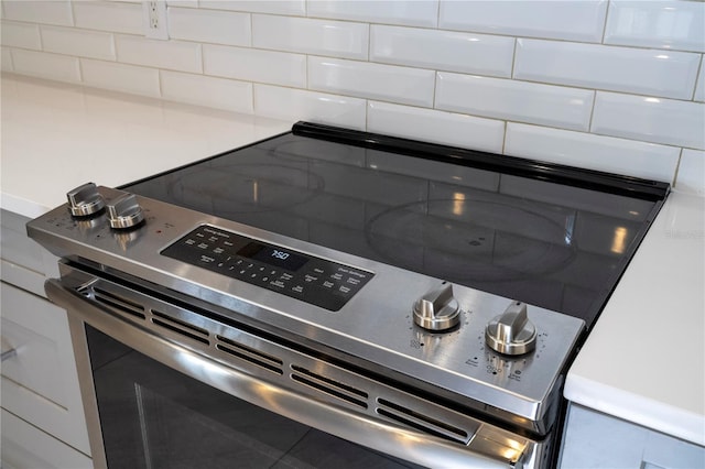 details featuring backsplash, stainless steel electric stove, and tile patterned flooring