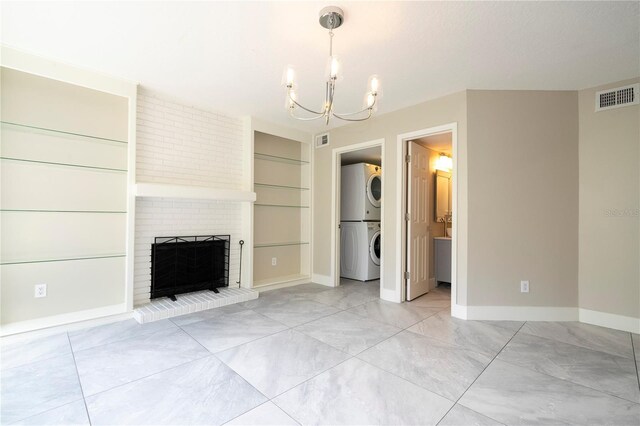 unfurnished living room with built in shelves, stacked washer / dryer, a brick fireplace, and a chandelier