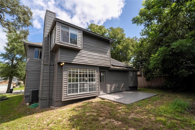 rear view of house featuring a patio, fence, a lawn, roof mounted solar panels, and a chimney