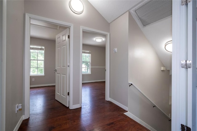 hallway with baseboards, visible vents, dark wood-type flooring, vaulted ceiling, and an upstairs landing