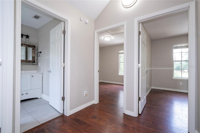 corridor featuring visible vents, baseboards, vaulted ceiling, and wood finished floors