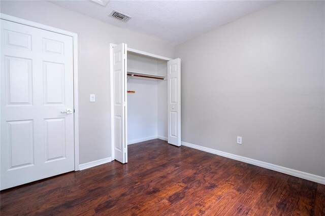 unfurnished bedroom featuring a textured ceiling, dark hardwood / wood-style floors, and a closet