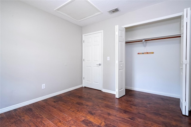 unfurnished bedroom with attic access, baseboards, visible vents, wood finished floors, and a closet