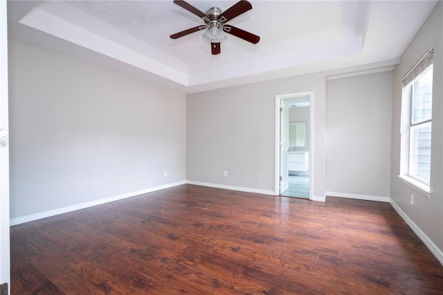 unfurnished room with dark wood-type flooring, a raised ceiling, a ceiling fan, and baseboards