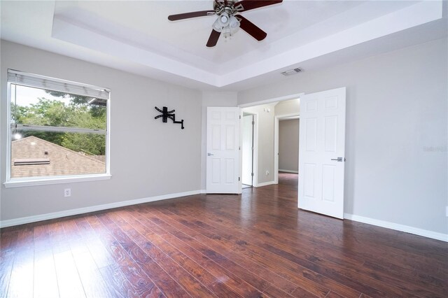 unfurnished room with dark wood-type flooring, a tray ceiling, and ceiling fan