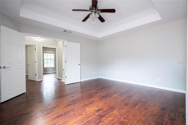 spare room with a raised ceiling, visible vents, baseboards, and hardwood / wood-style flooring