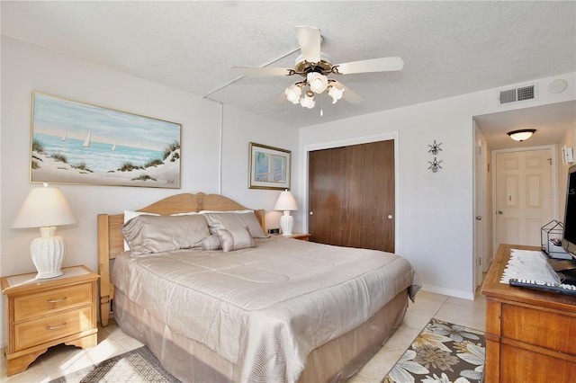 bedroom with light tile patterned flooring, ceiling fan, a closet, and a textured ceiling