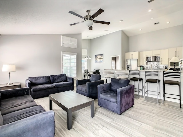 living room with ceiling fan, light wood-style floors, visible vents, and high vaulted ceiling