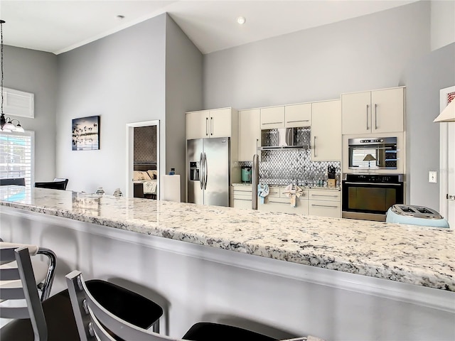 kitchen featuring decorative light fixtures, light stone countertops, stainless steel appliances, decorative backsplash, and a towering ceiling