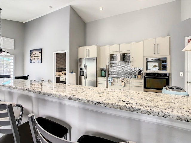 kitchen featuring backsplash, multiple ovens, a kitchen bar, light stone counters, and stainless steel fridge