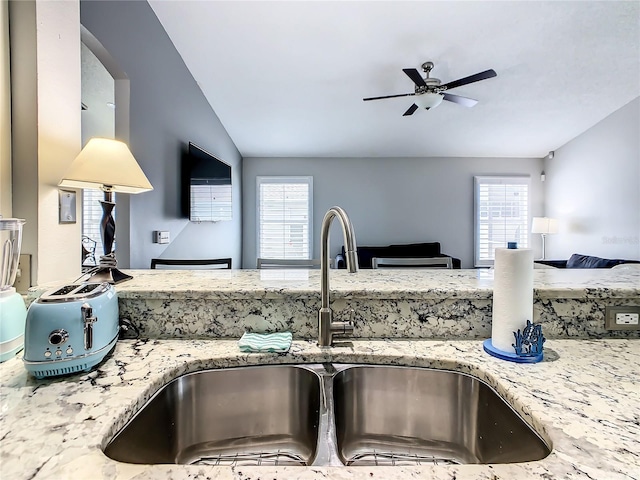 kitchen with a sink, plenty of natural light, open floor plan, and light stone countertops