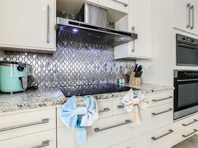 kitchen featuring light stone counters, extractor fan, black appliances, white cabinetry, and tasteful backsplash