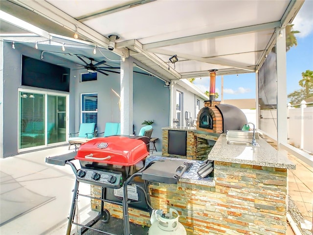 view of patio / terrace featuring area for grilling, a ceiling fan, a sink, fence, and exterior kitchen