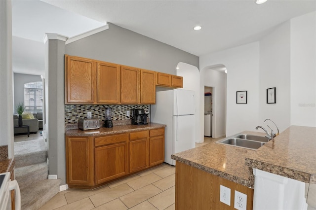 kitchen with light tile patterned floors, tasteful backsplash, kitchen peninsula, sink, and white refrigerator